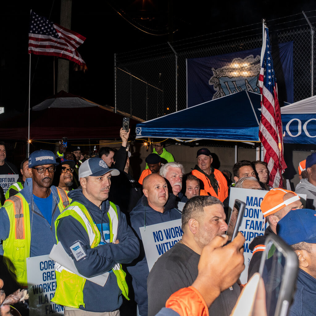 A large group of striking union members gathering in front of a railroad crossing sign.