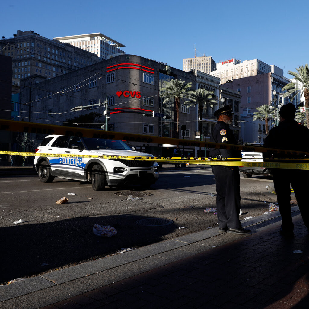 Police officers stand behind strips of caution tape on a street in New Orleans.