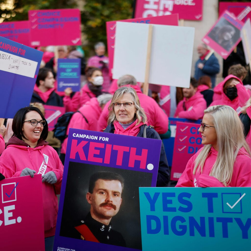 A crowd of people, many of whom wearing pink and carrying signs. One in the middle has a sign reading “Campaign for Keith,” and bearing the image of a man in a militarylike uniform.