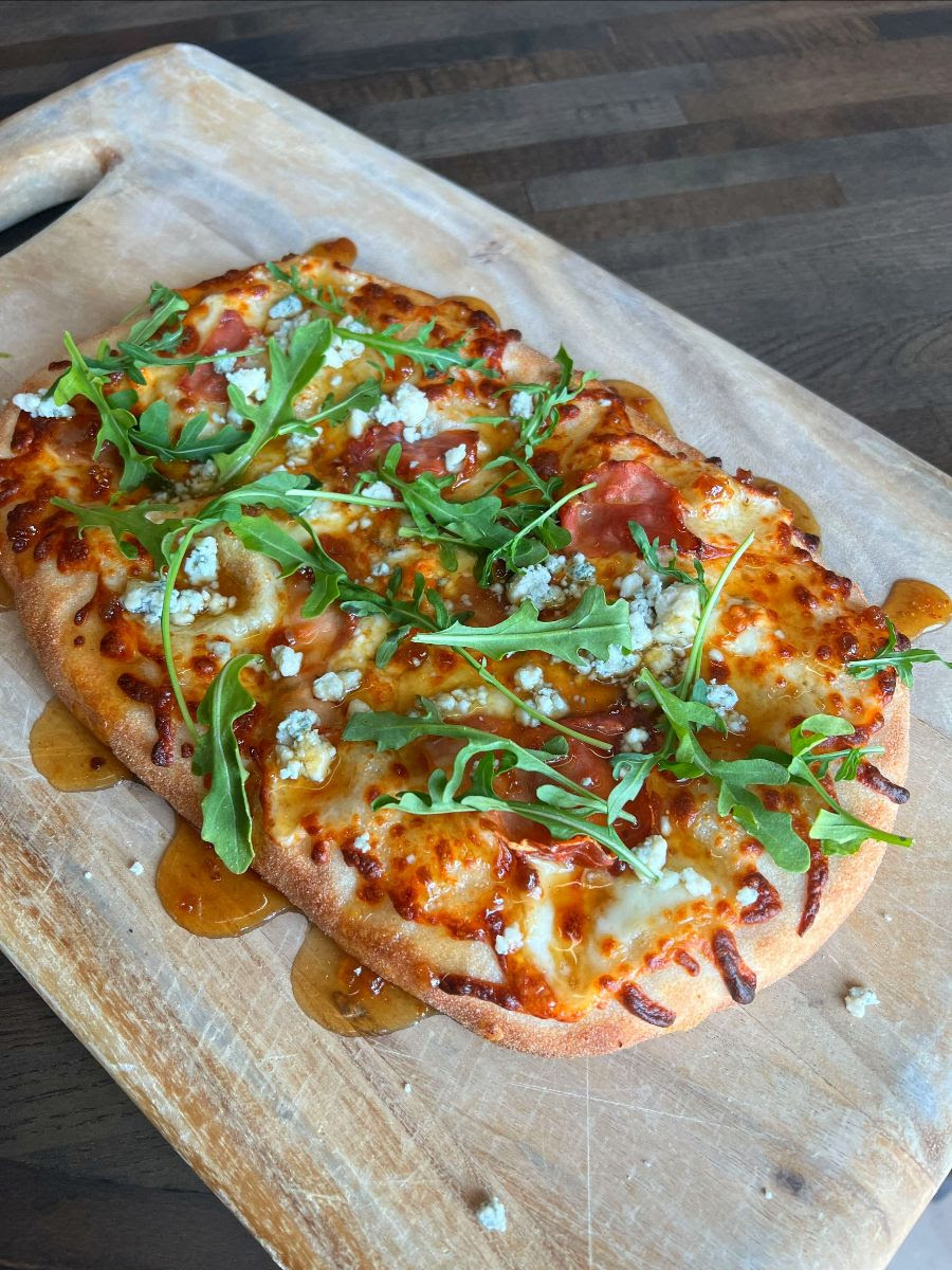 A picture of Figgy Bleu Flatbread topped with fresh arugula and blue cheese crumbles with Code 3 Fig sauce.