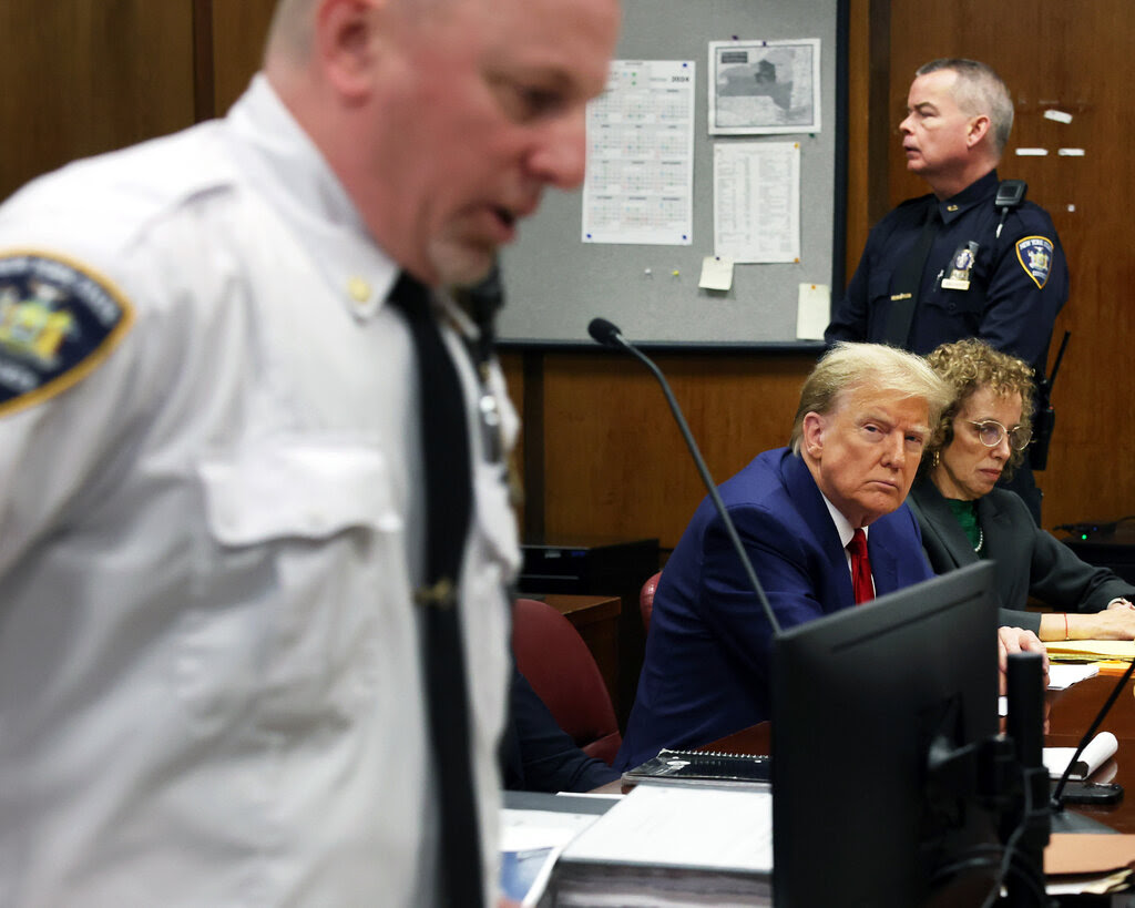 Former President Donald Trump in a blue suit, red tie and white shirt sitting inside a courtroom.