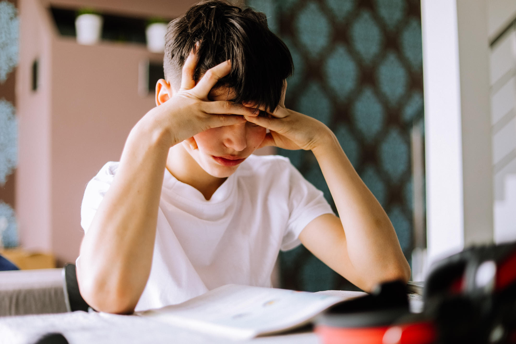 A teenage boy is concentrated diligently sitting and reading a book with his head supported by his hands.
