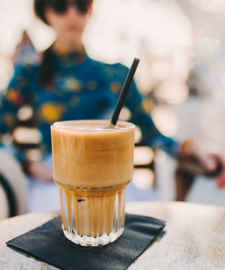 Jeune femme assise à une table pour boire un frappé vanille Nescafé en été. 