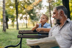 little boy blowing the soap bubbles in the park with his grandfather