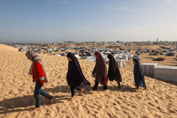 Palestinian girls walk on a sand dune toward a tent dedicated to Qoran reading, at a camp for displaced people in Rafah in the southern Gaza Strip on March 17