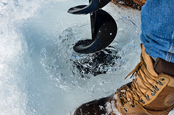 An ice angler pulls an auger back through the ice after drilling a hole for fishing.