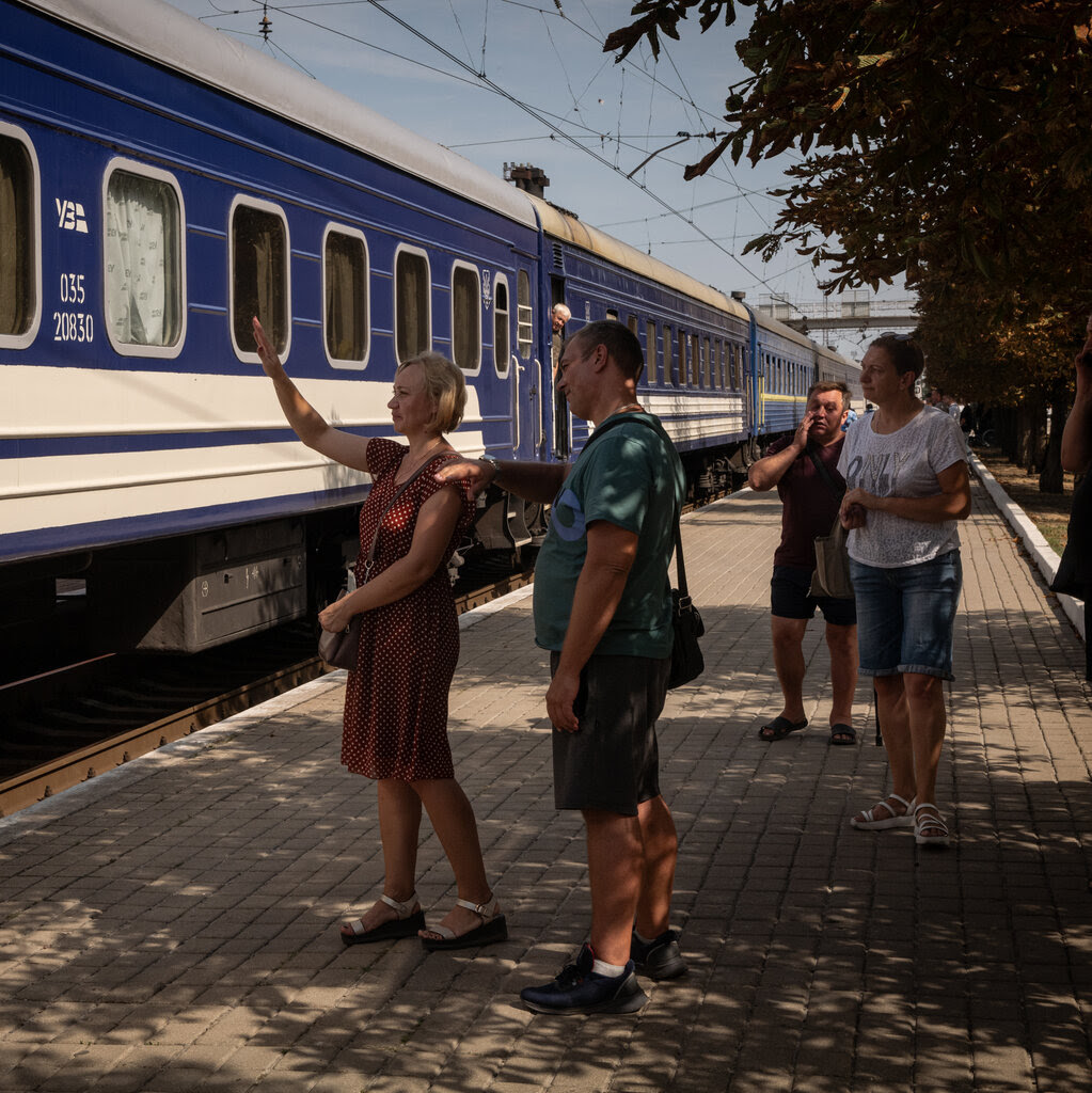 Four people stand as a train prepares to leave a station. One of them is waving. 