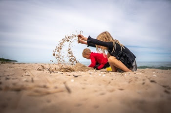 A little girl and little boy crouch down on the beach at Hoeft State Park as they dig through the sand, sending sand up in the air