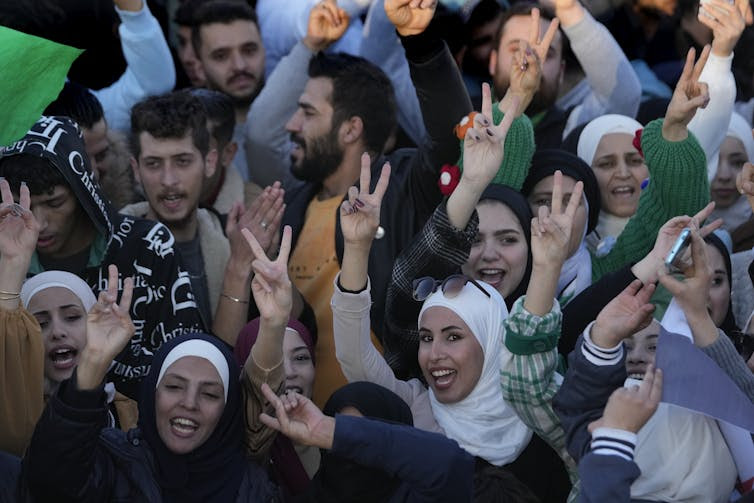 Men and women smile, hold up V signs and celebrate in a city square.