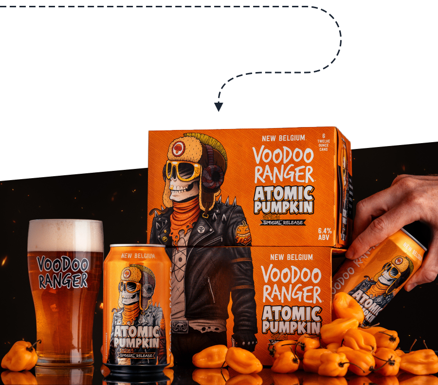 Promotional display for New Belgium's Voodoo Ranger Atomic Pumpkin Spicy Special Release beer. A six-pack of cans is featured in the center, with bold orange packaging depicting the signature skeleton character dressed in a black leather jacket and aviator hat with goggles. A pint glass filled with the amber-colored beer sits to the left, branded with the Voodoo Ranger logo. To the right, a hand is seen grabbing a can from the six-pack, with bright orange habanero peppers scattered in front of the display, reflecting the beer’s spicy flavor profile.