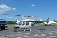 A helicopter parked on a paved landing pad with greenery in the background