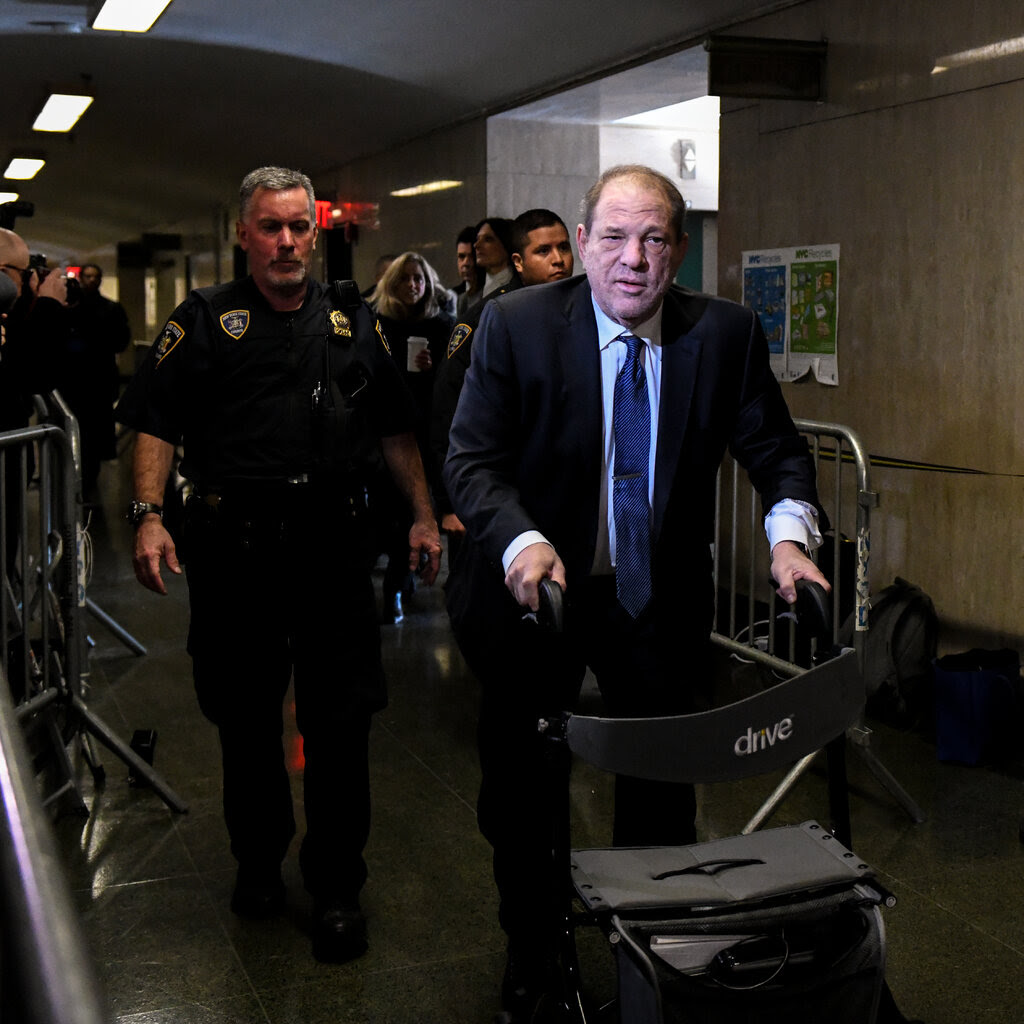 Harvey Weinstein, in a suit and tie, walks with a walker. 