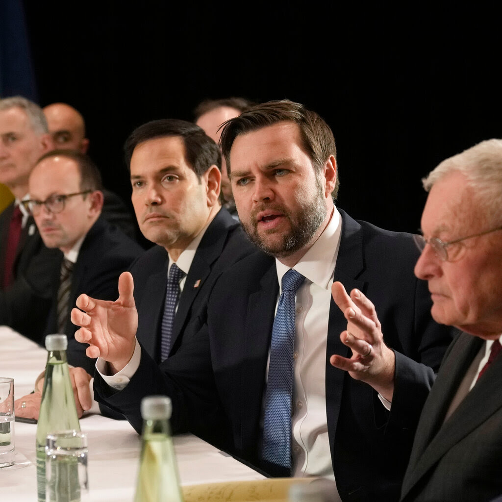 A man speaks at a table full of other men. 