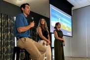 Dr. Gus Alaka speaking on stage during a panel next to the facilitator Bianca Sproul, and another panel member to her right.