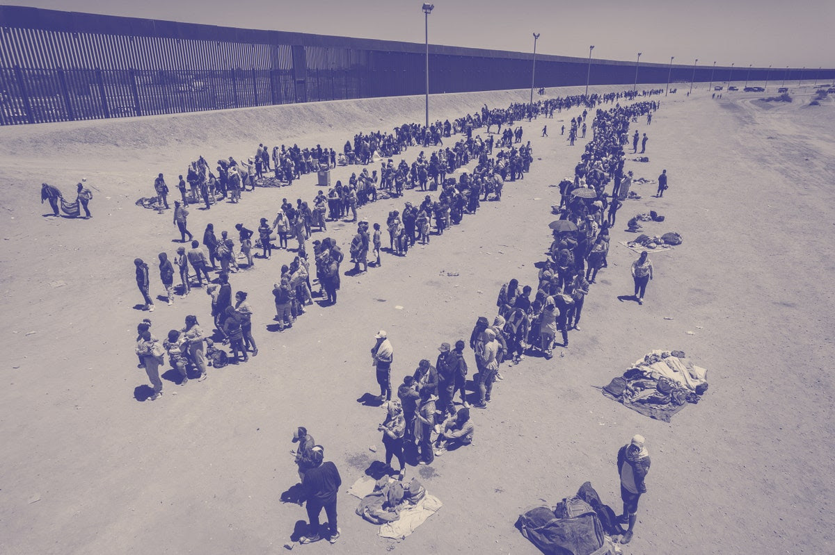 A large group of people standing at the U.S. -Mexico border.