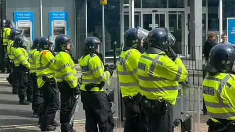 Police officers with riot shields and protective helmets standing in a line separating protesters