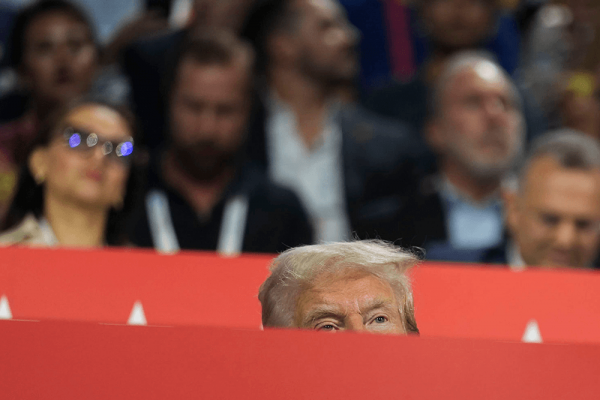 The top half of Donald Trump's head is seen behind red barrier. A crowd stands behind him. 