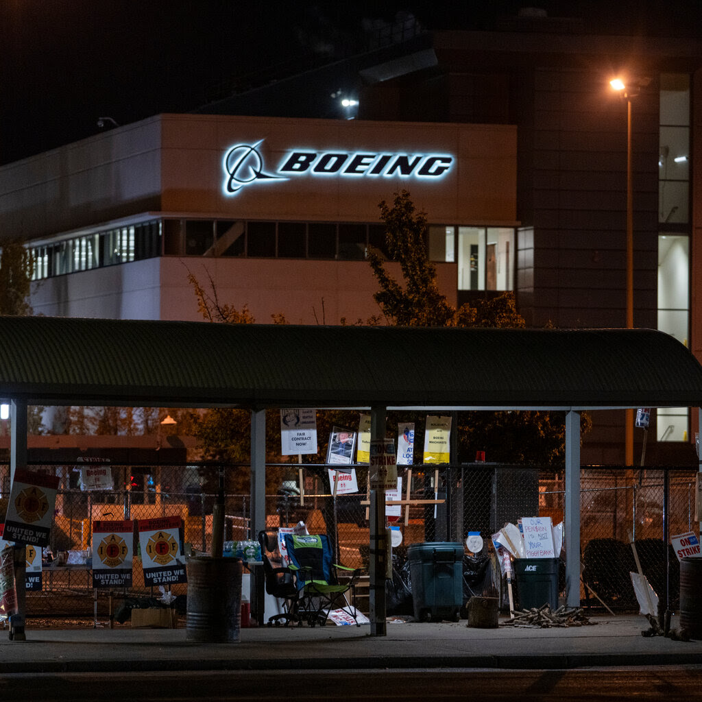 A building at night with an illuminated Boeing logo. In front of it is an area with a bunch of abandoned picket signs.