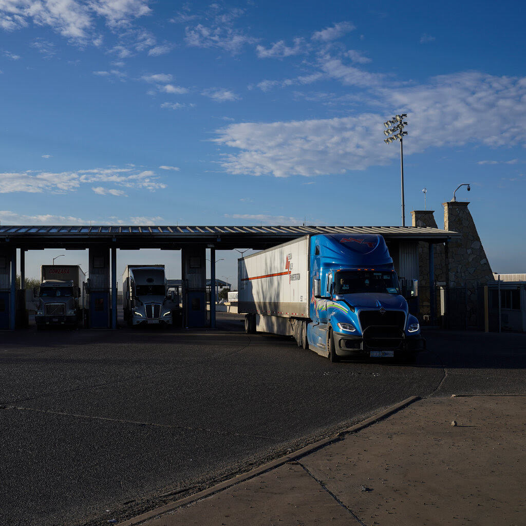 Trucks passing through a station under a blue sky.