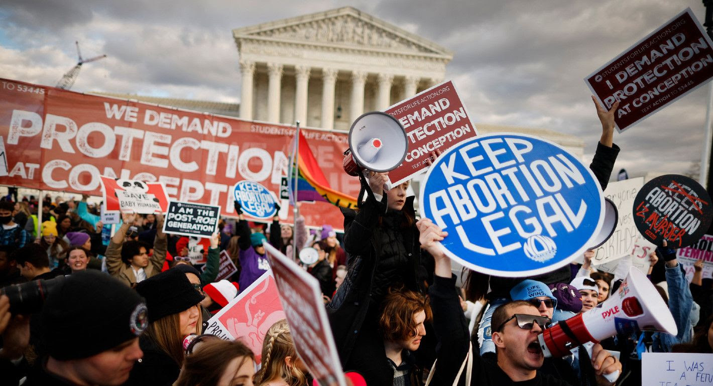 Photograph of a pro-choice protester holding a sign reading "keep abortion legal" as anti-abortion campaigners in the background participate in the "March for Life" outside the U.S. Supreme Court.