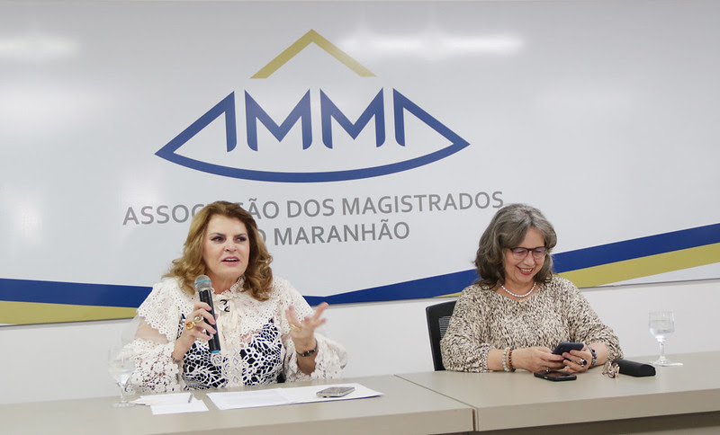 Foto colorida mostra duas mulheres sentadas em uma mesa durante solenidade de encerramento da Semana de Justiça Restaurativa.