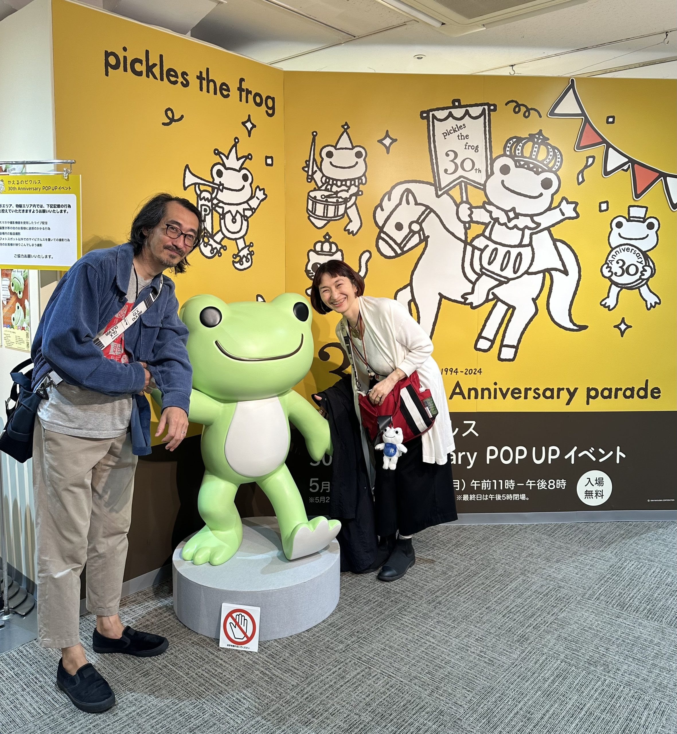 カエルのピクルスのフィギュアと一緒にいる佐藤安南と夫、松屋銀座のポップアップイベント会場にて