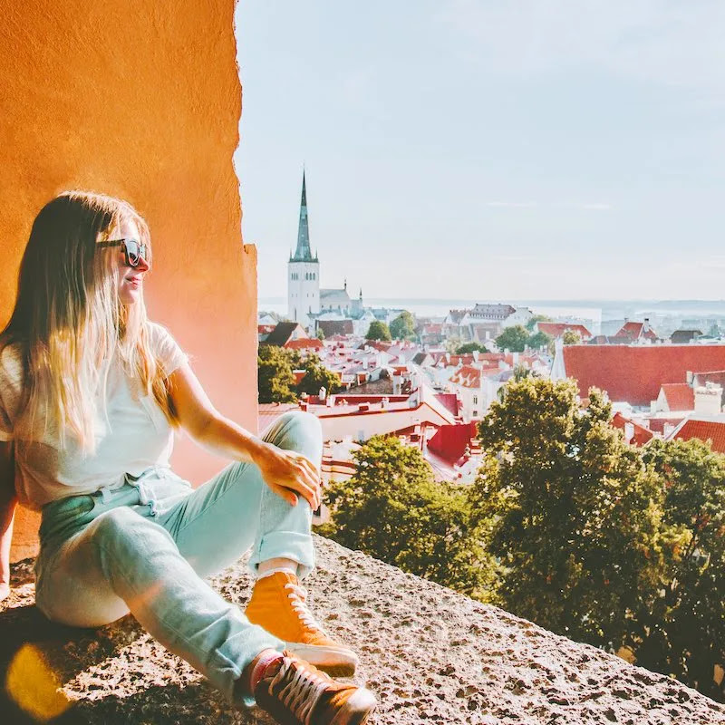 Woman Sitting On The Parapets Overlooking Old Town Tallinn, The Capital City Of Estonia, Baltic Coast Of Northern Europe