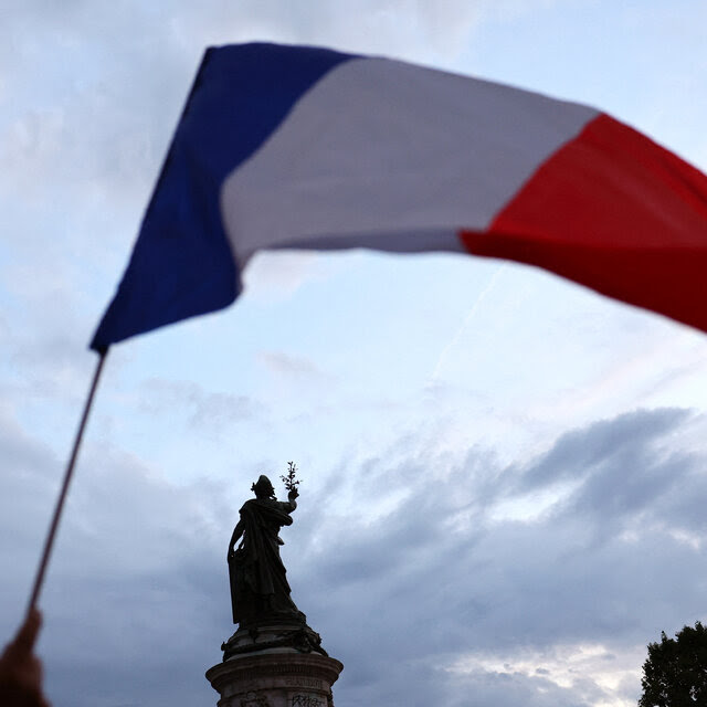 A French flag is hoisted in the air. In the background is a statue. 