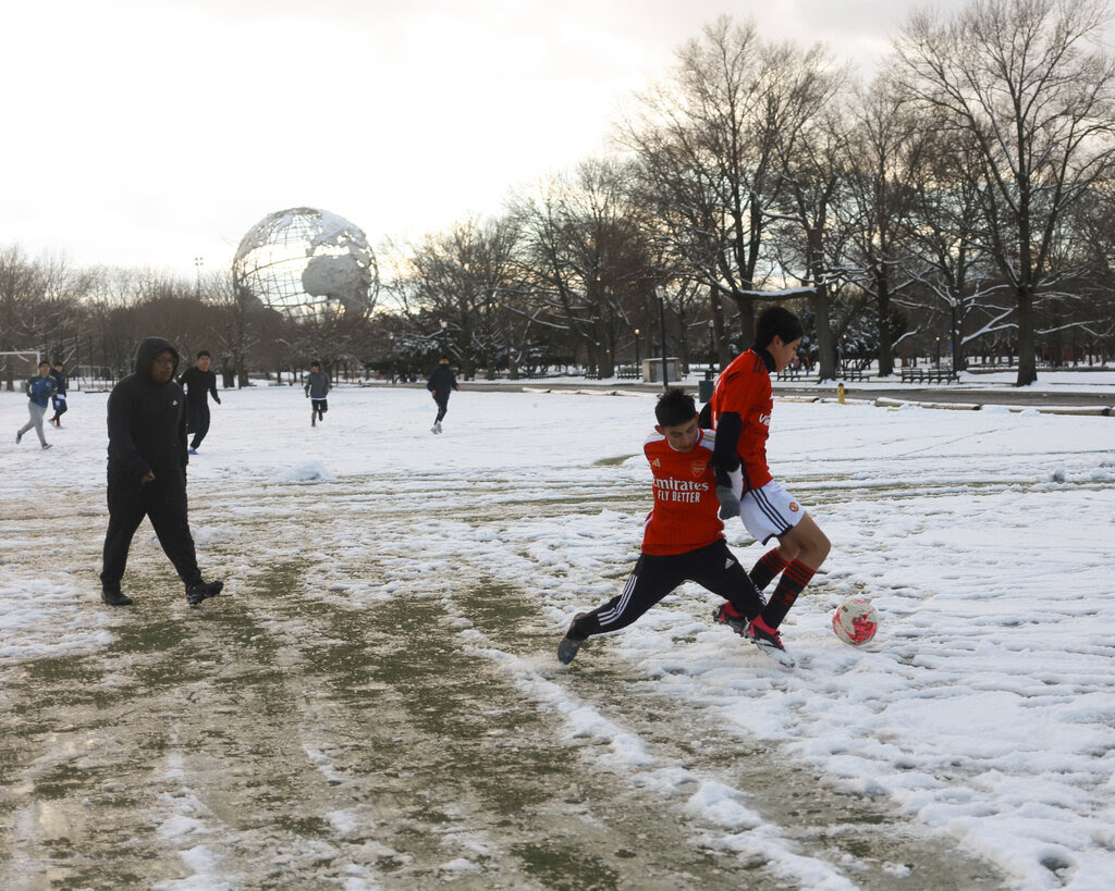 Two men in red jerseys grapple over a soccer ball on a field covered in snow.