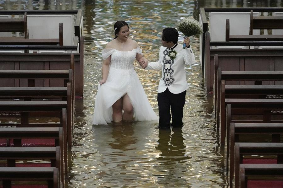 A newlywed couple hold hands and walk down the aisle at a flooded church in the Philippines. The water comes up to their knees and the pews of the church are empty.