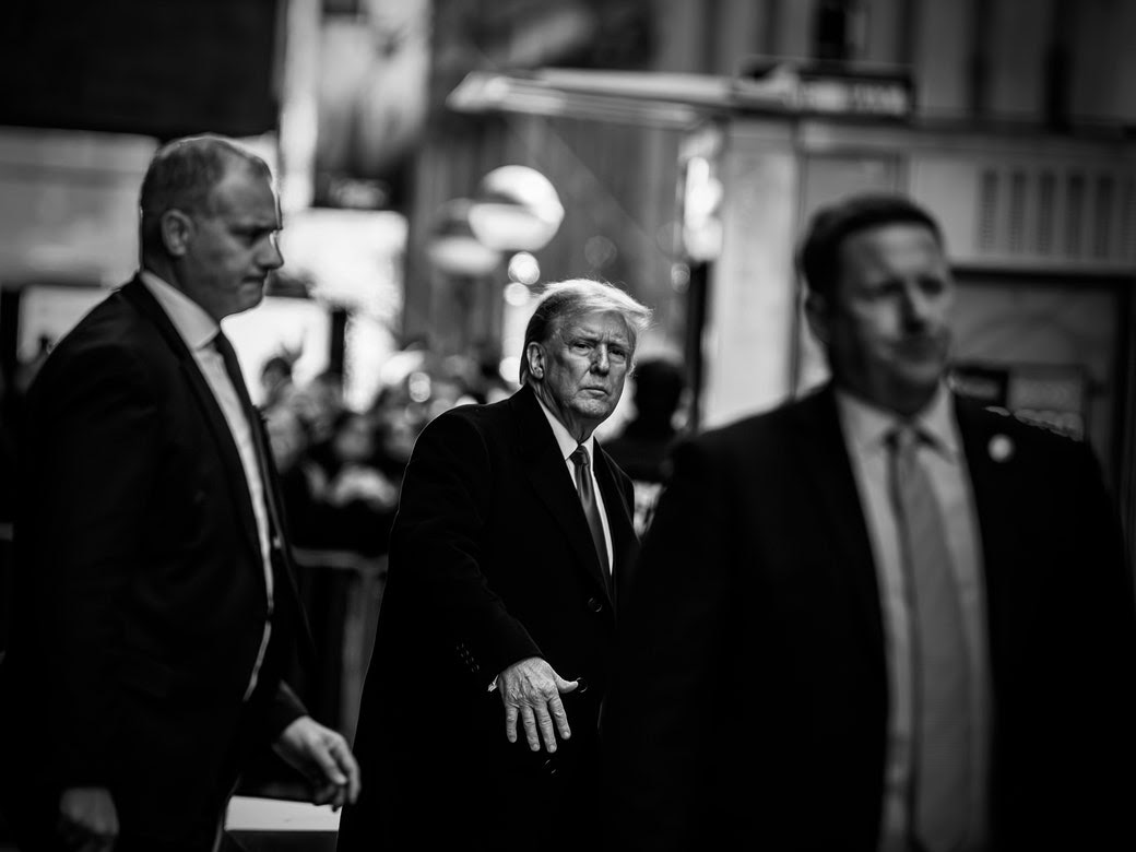 A black-and-white photo of the former President Donald Trump, getting into a car outside of a Manhattan courtroom.