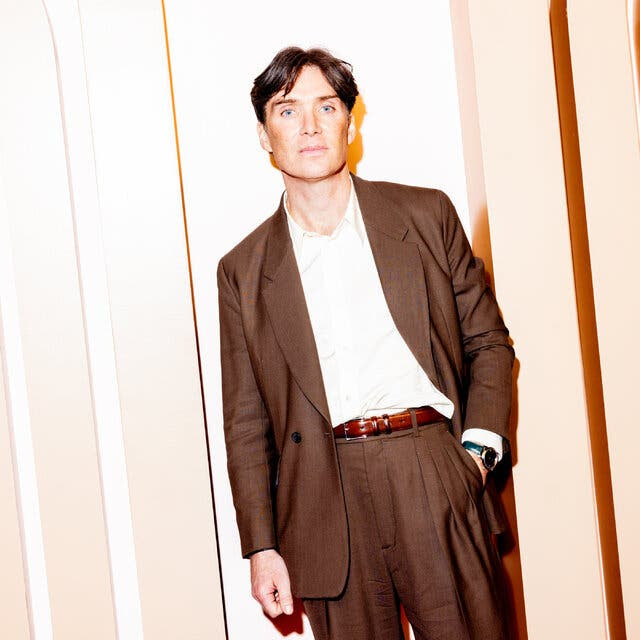 Cillian Murphy posing in a loosefitting brown suit and a white button-up shirt with no tie.