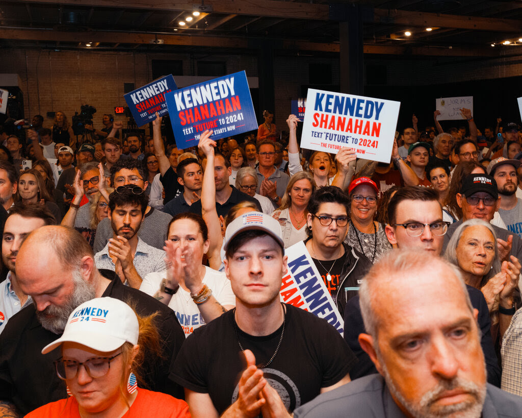 Supporters of Robert F. Kennedy Jr. and his running mate, Nicole Shanahan, at a rally. Many are holding signs with the candidates’ names. 