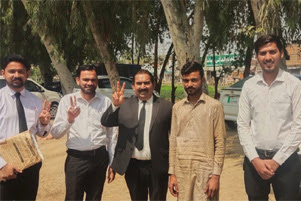 Five men are standing outside. Most are smiling.