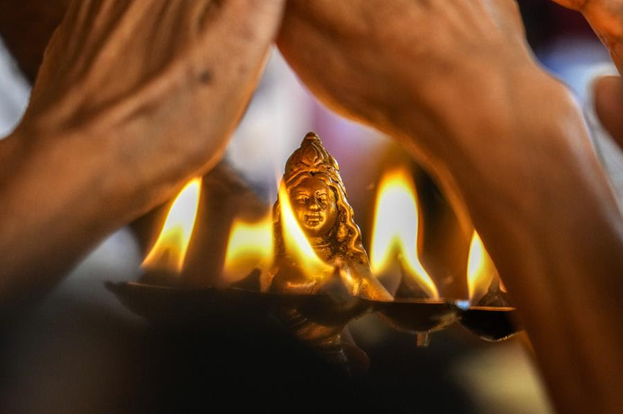 A traditional oil lamp that is burning. There is a small golden statue of the Hindu goddess Durga.