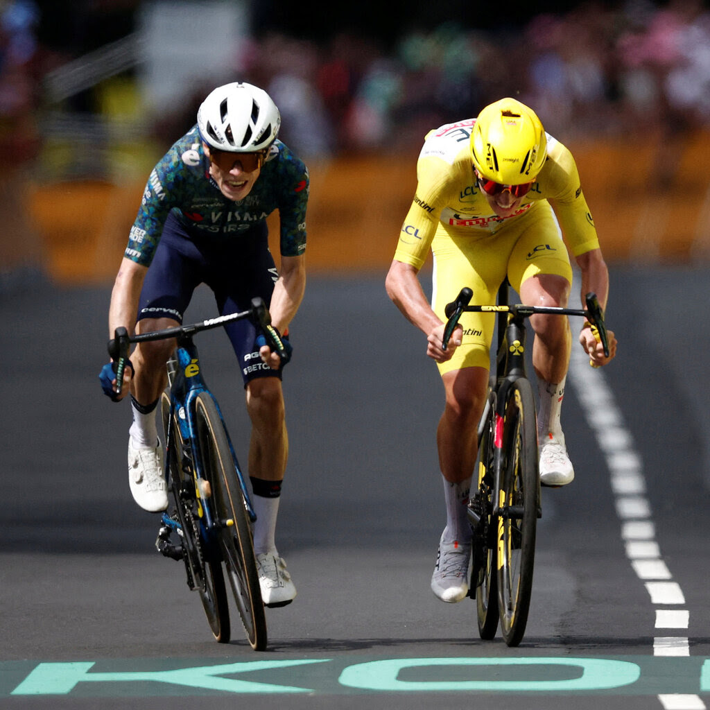 Jonas Vingegaard stands up out of his bicycle saddle while racing on an asphalt road against Tadej Pogacar, who is wearing yellow.