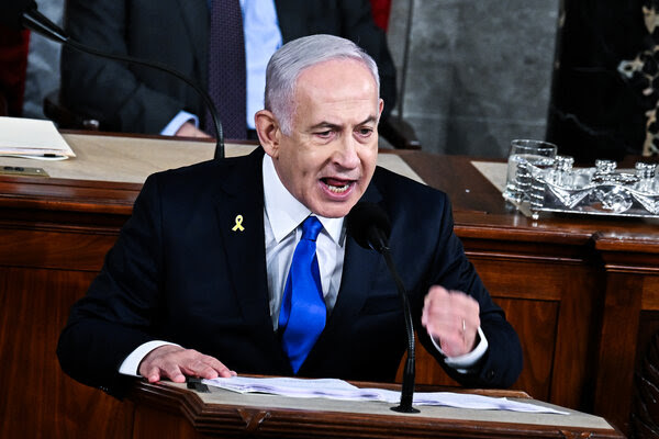 Benjamin Netanyahu se tient debout sur une estrade et lève le poing. Il porte un blazer bleu marine et une cravate bleue.