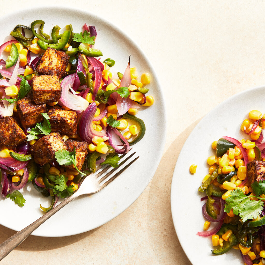 A plate with tofu, corn, chiles, red onions and leafy herbs.