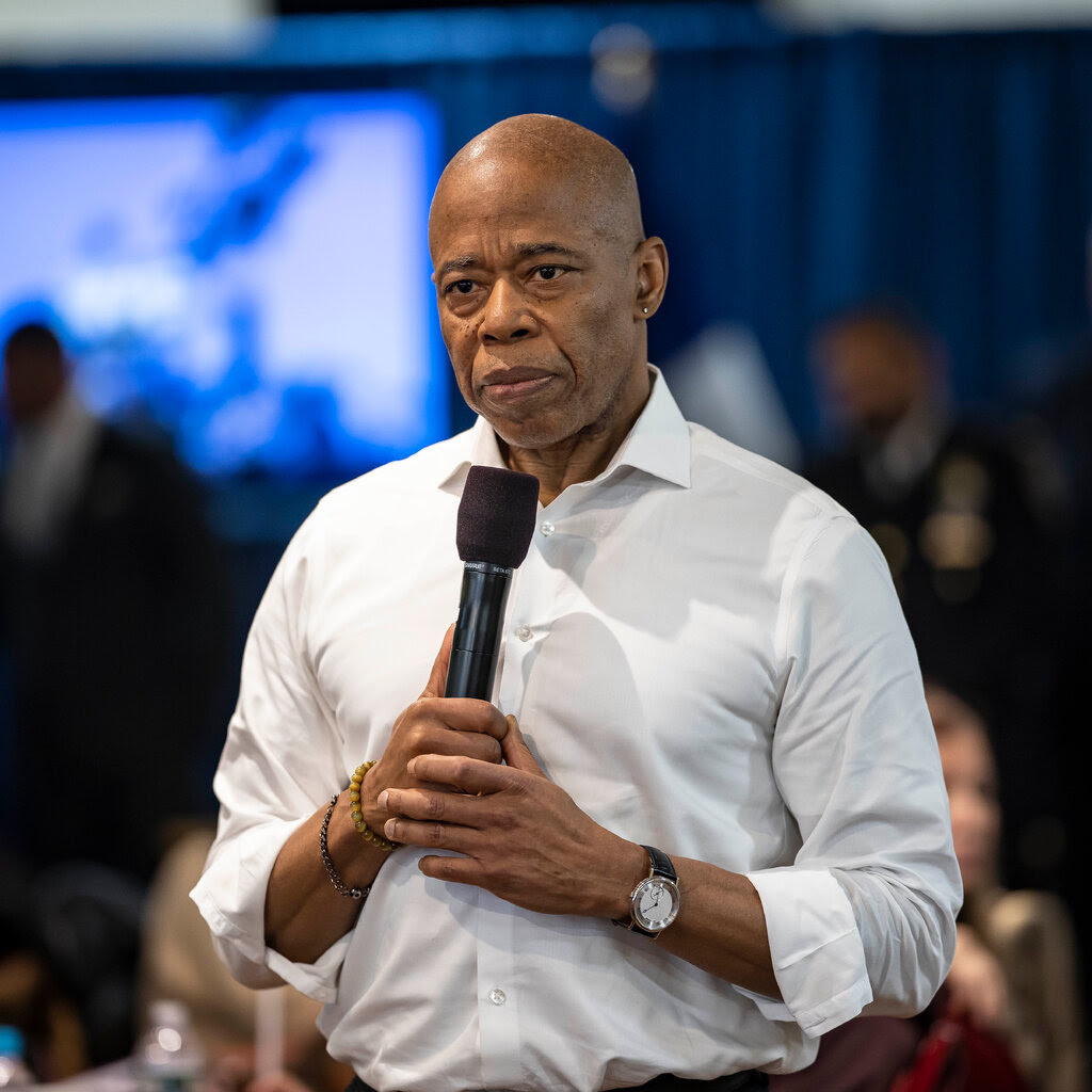 A man in a white shirt holds a microphone. 