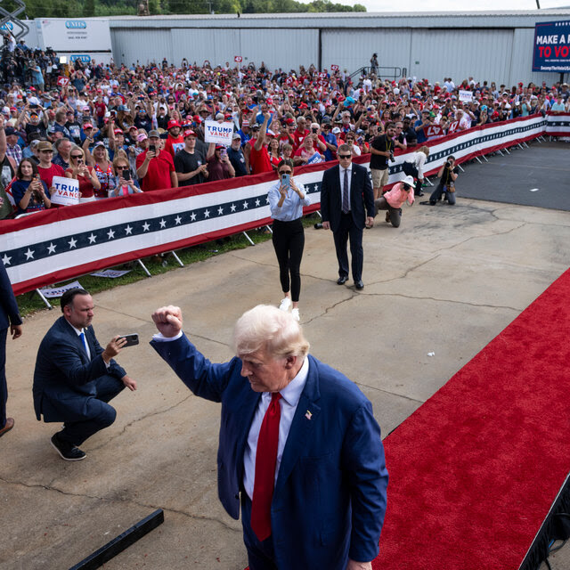 Donald Trump raising a fist in the air as he walks off an outdoor stage surround by a large crowd.