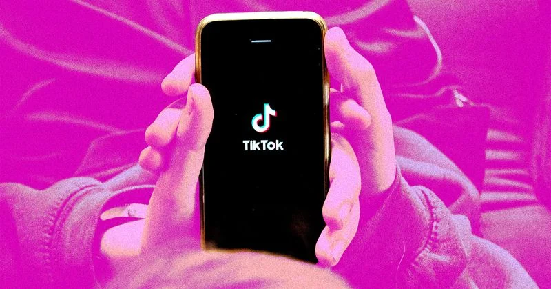 Person holding a phone with the Tik Tok logo on the screen and a pink overlay effect