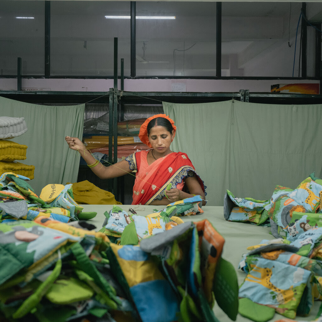 A woman wearing an orange cap and a blue, peach and orange sari with embroidered details stitches plush toys at a factory in India. 