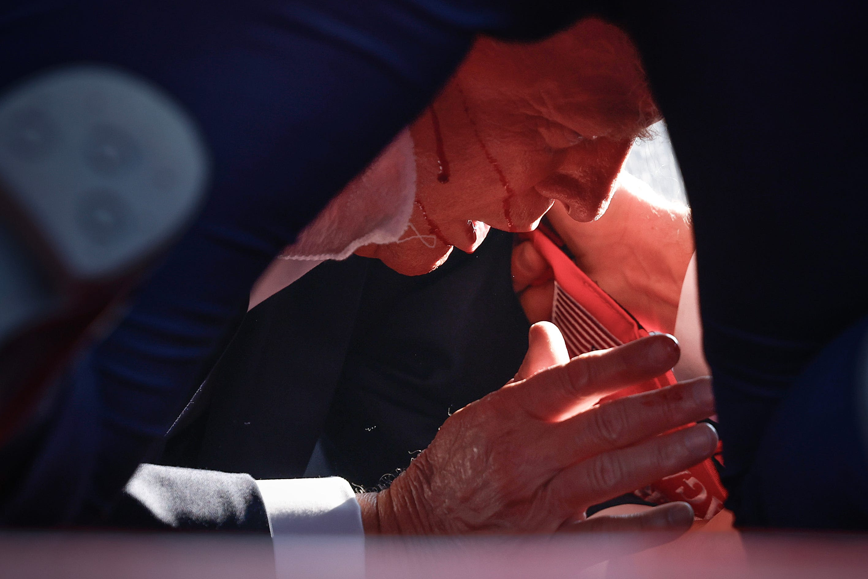 Trump covered by Secret Service agents, with blood lines running across his face.