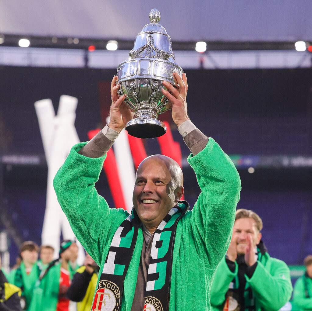 A bald man in a bright green fleece hoists a silver trophy.