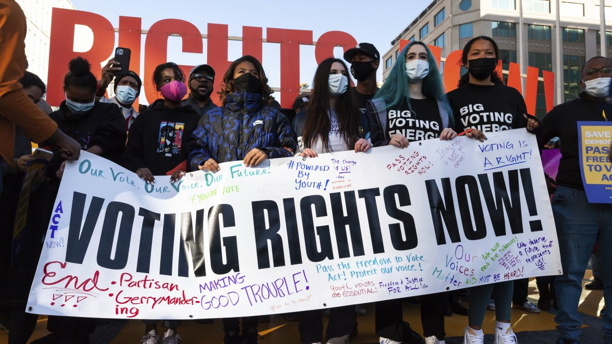 A group of people march and hold a sign that reads ''voting rights now''