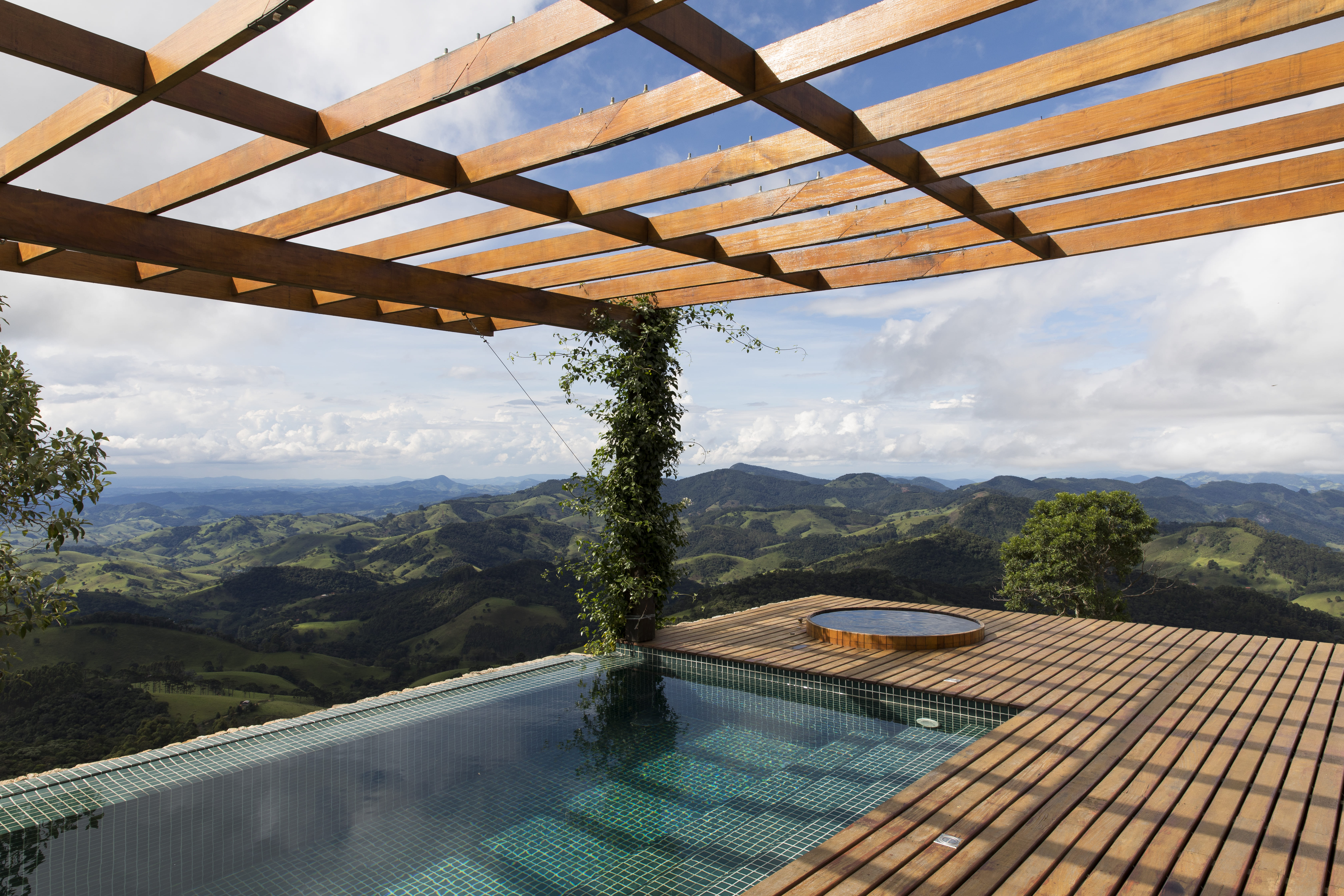 O pátio central da casa, neste projeto da Sabella Arquitetura, apresenta uma piscina de borda infinita, criando a ilusão de água sem fim. Cercada por um deck de madeira e áreas de estar confortáveis, oferece um local ideal para relaxar e apreciar a natureza | Fotos: Maíra Acayaba 