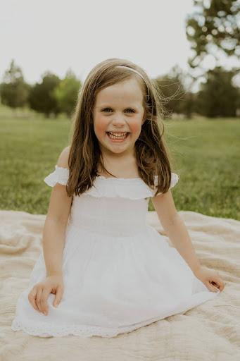 Picture of a little girl in a white dress with a big smile. 