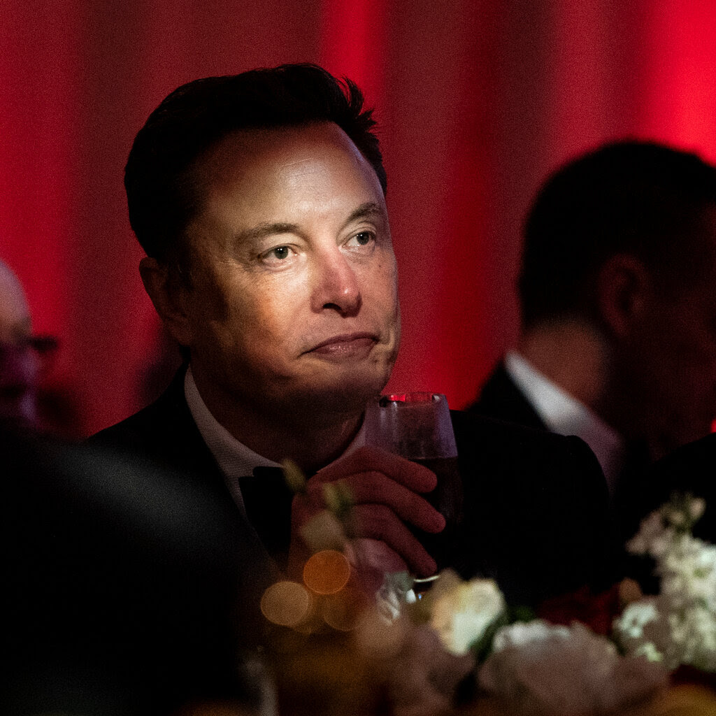 Elon Musk holding a glass in a suit. 