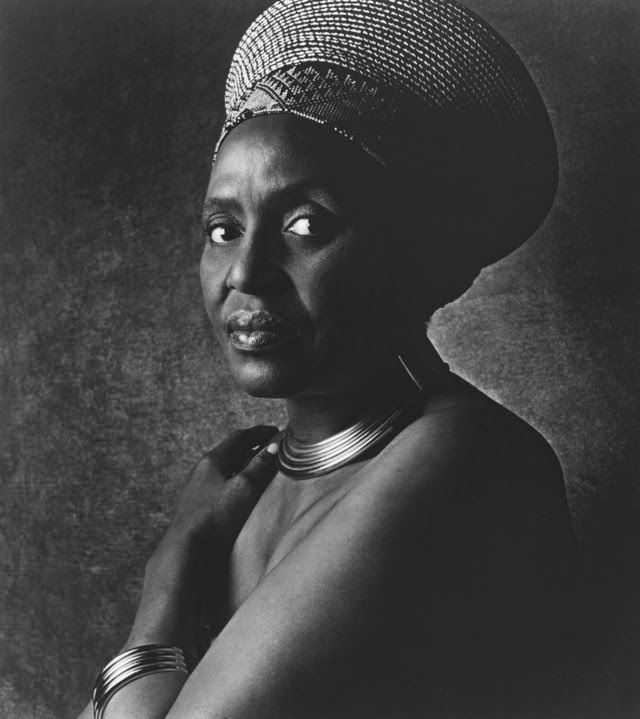 Singer and activist Miriam Makeba, bare-skinned except for some traditional African jewellery, looks to her left at the camera with an expression of dour intensity.