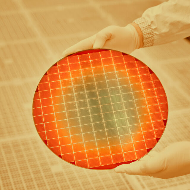 The photograph portrays a gleaming disc, red, orange and yellow, held in white-gloved hands.